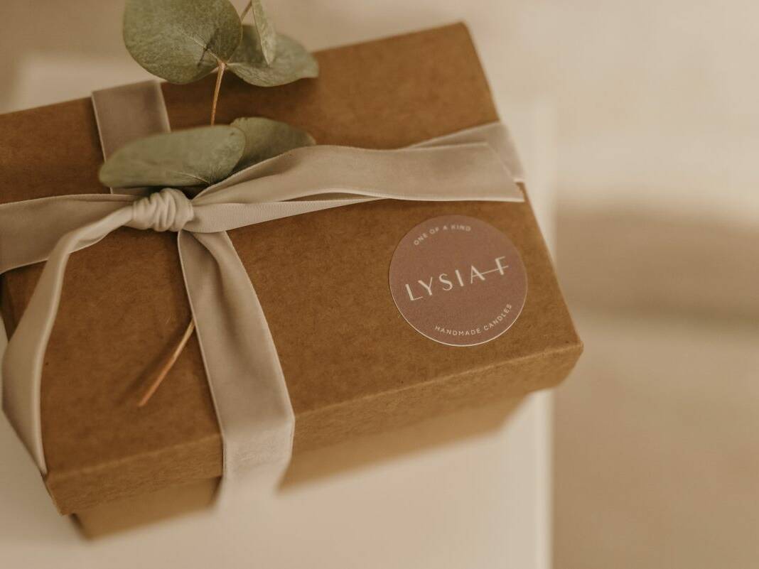 Lysia–F Produkt-Kartonverpackung mit beiger Schleife, Blume und mit Logo-Sticker.