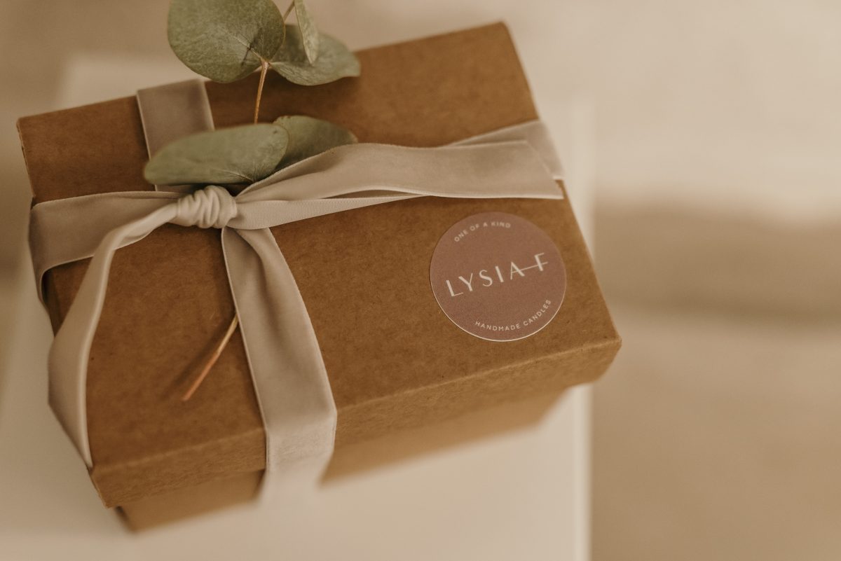 Lysia–F Produkt-Kartonverpackung mit beiger Schleife, Blume und mit Logo-Sticker.