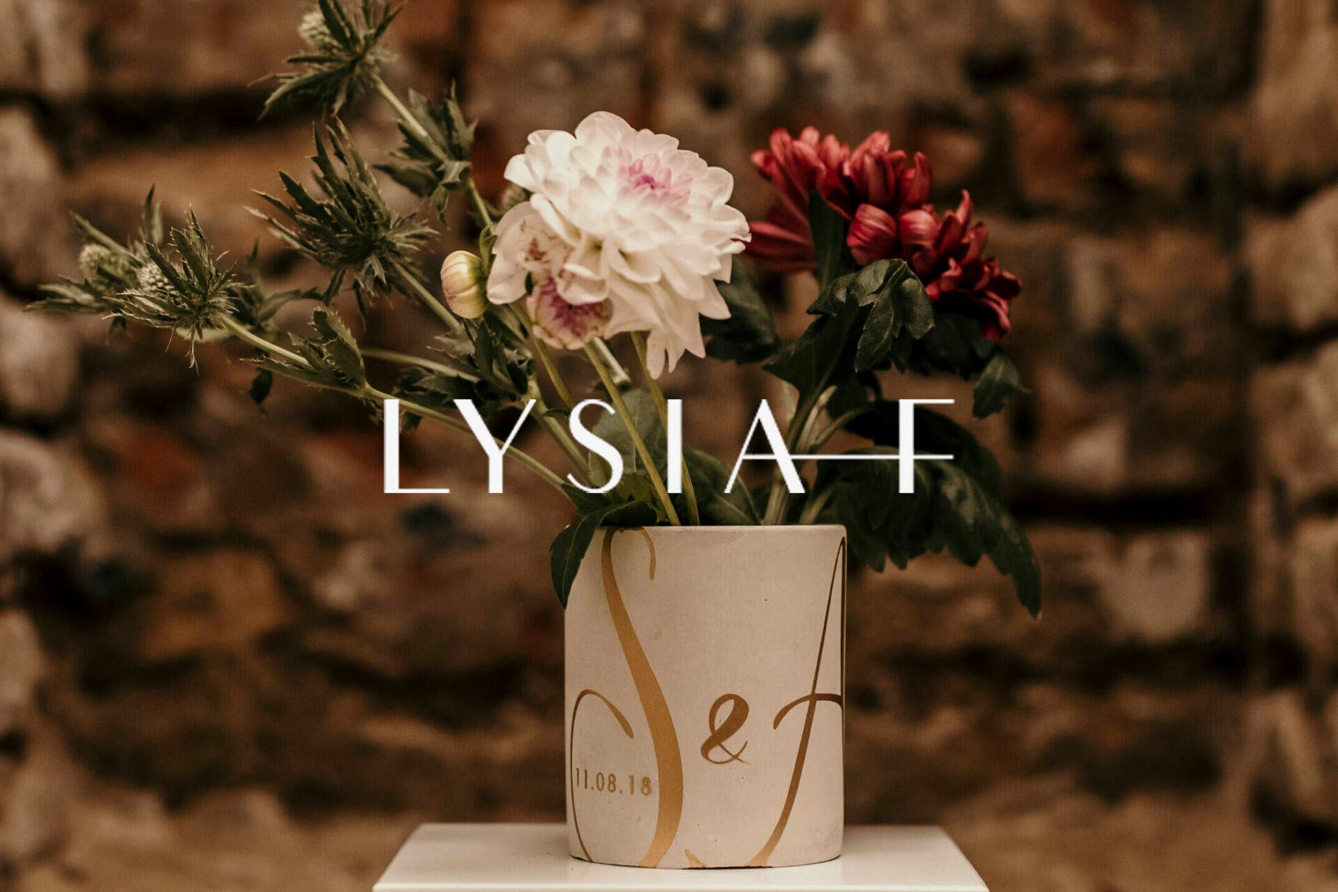 LYSIA–F Logo. Im Hintergrund eine Hochzeitskerze gefüllt mit roten und weißen Blumen.