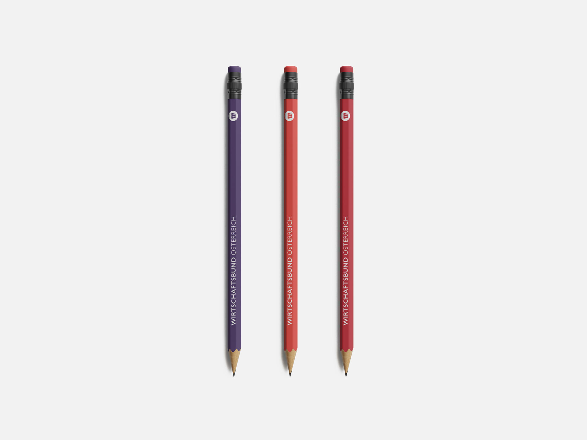 Drei nebeneinanderliegende Bleistifte mit Radiergummi in violett, rot und orange mit Wirtschaftsbund-Logo und Schriftzug.