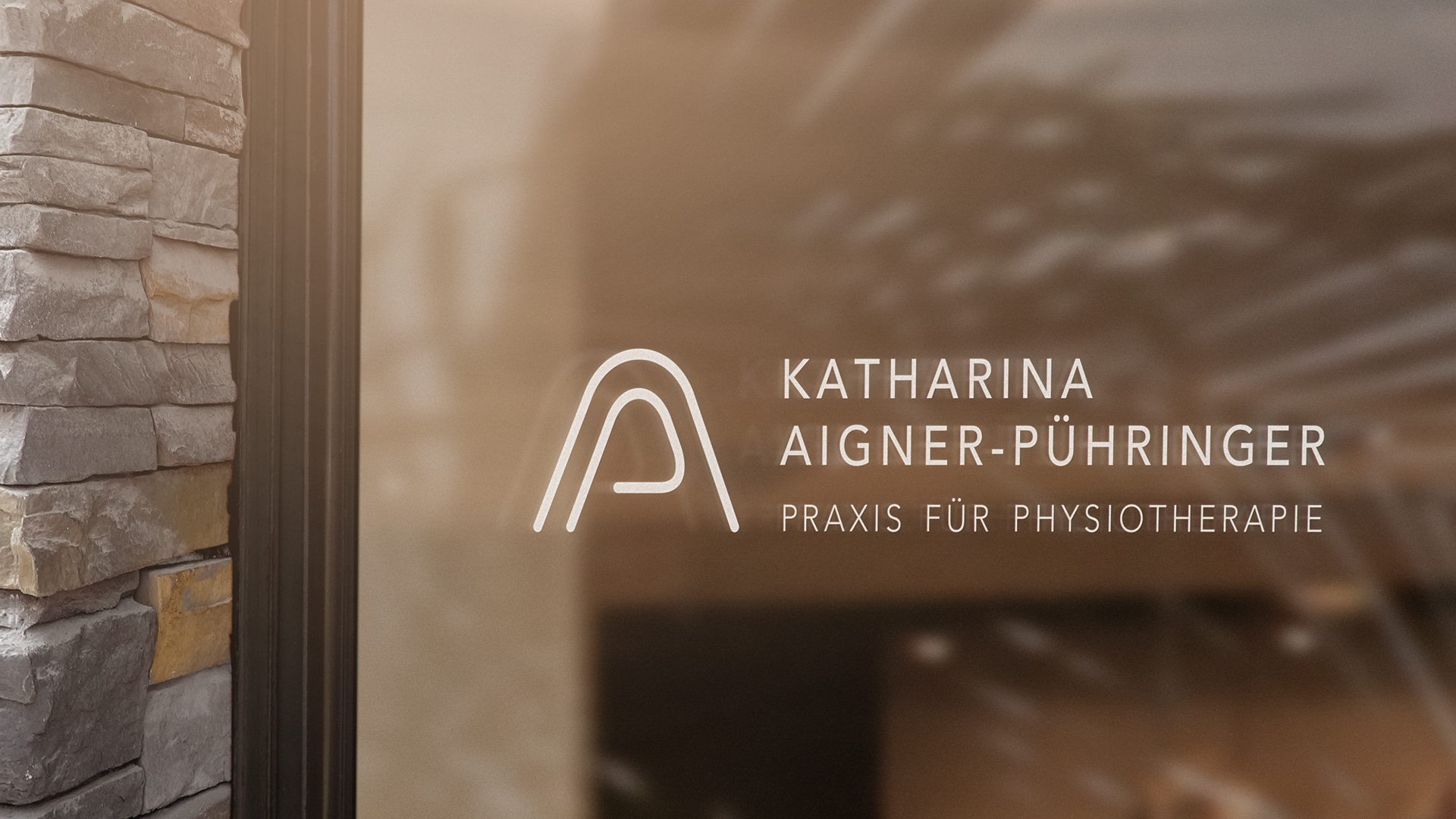 Logo mit Schriftzug der Praxis für Physiotherapie von Katharina Aigner-Puehringer abgebildet auf der Scheibe eines Schaufensters der Praxis.