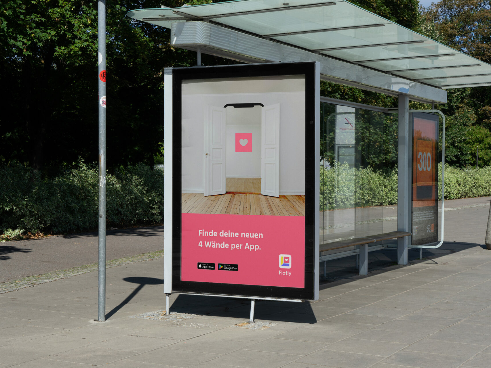 Plakatwerbung mit der Aufforderungen die Flatly-App herunterzuladen. Das Plakat ist an einer Bushaltestelle in Form eines Citylights montiert.