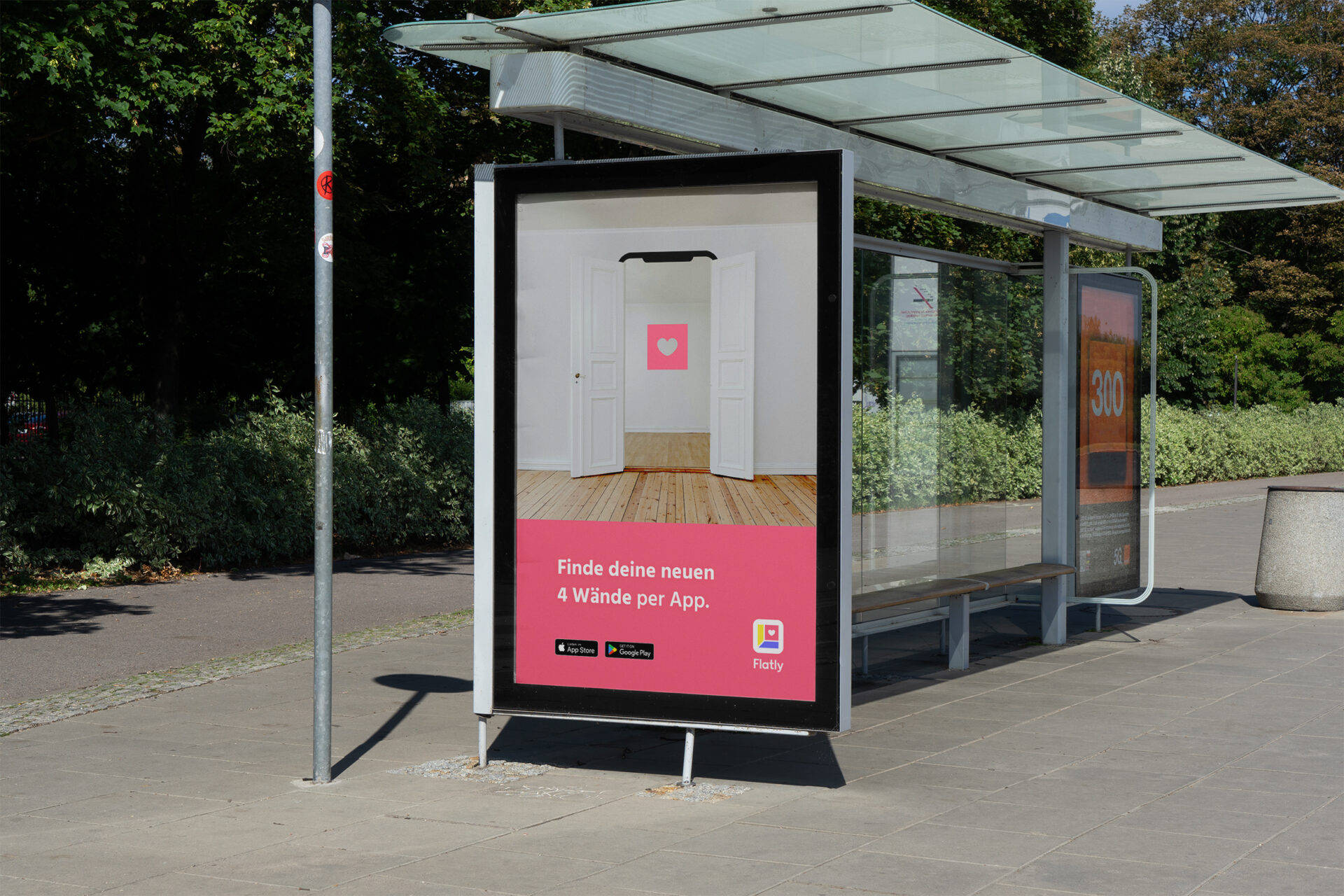 Plakatwerbung mit der Aufforderungen die Flatly-App herunterzuladen. Das Plakat ist an einer Bushaltestelle in Form eines Citylights montiert.